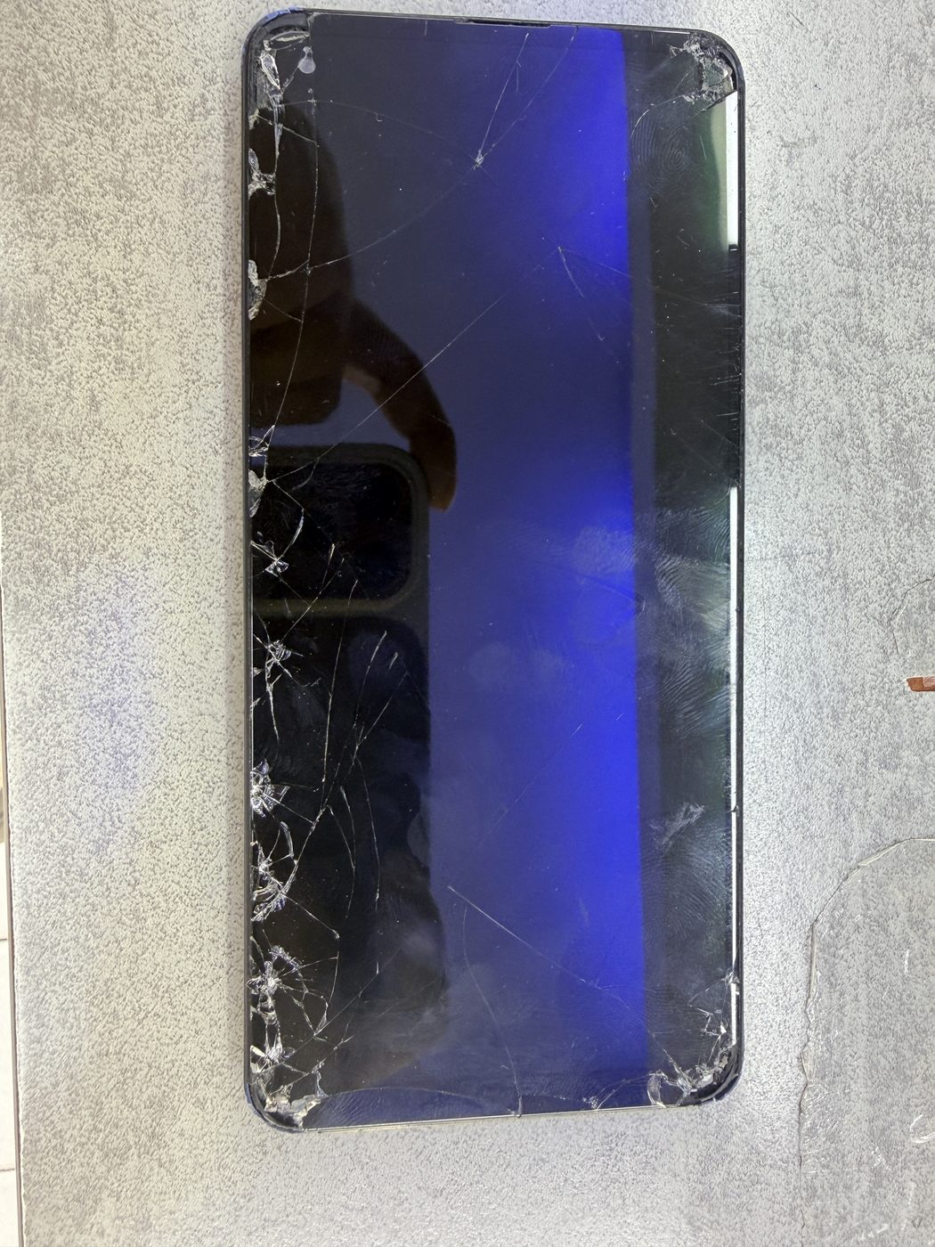 iPhone avec écran fissuré posé sur un tapis de réparation