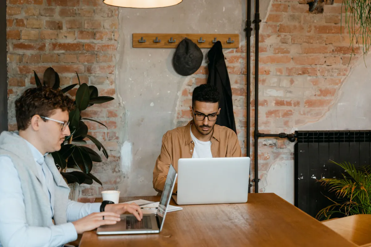 Two small-business colleagues comparing cloud provider options on their laptops in a workspace with an exposed brick wall