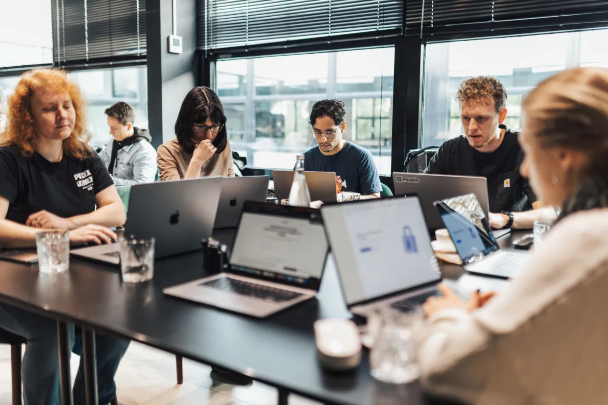 Six people around a meeting table with open laptops, in a bright office