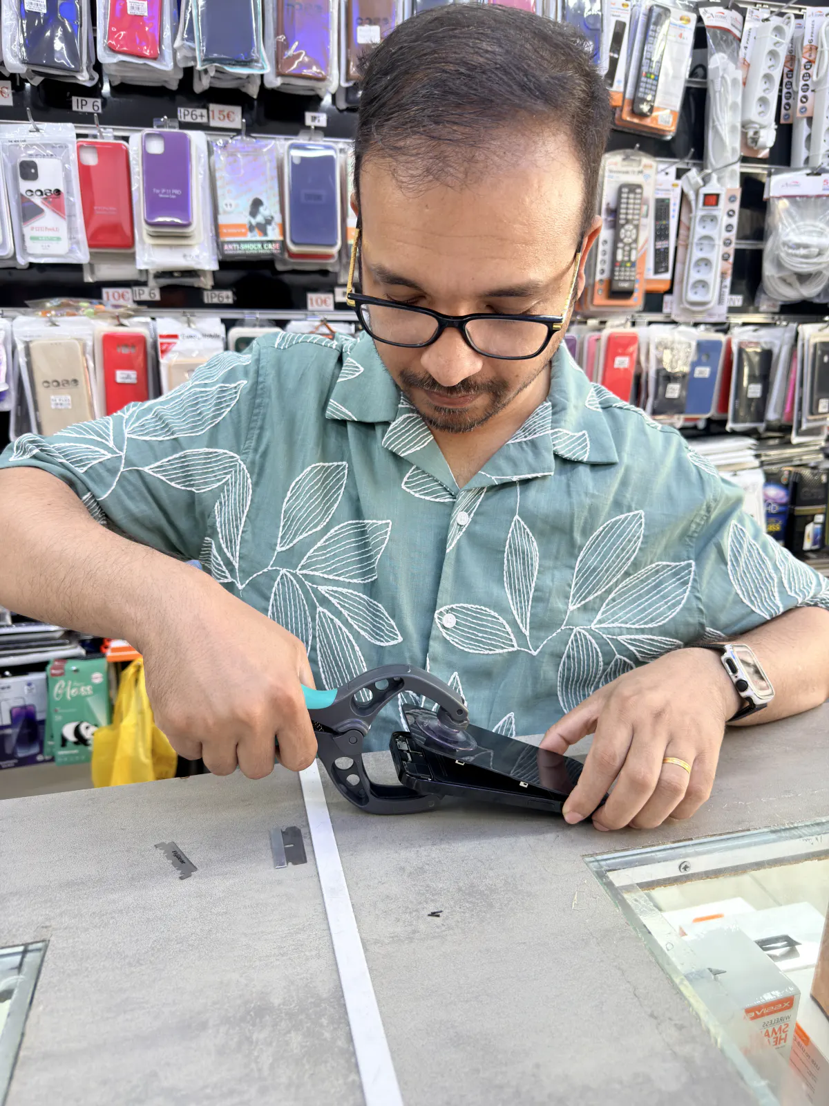 Technician using a double-suction-cup plier tool to lift a smartphone screen at the repair counter