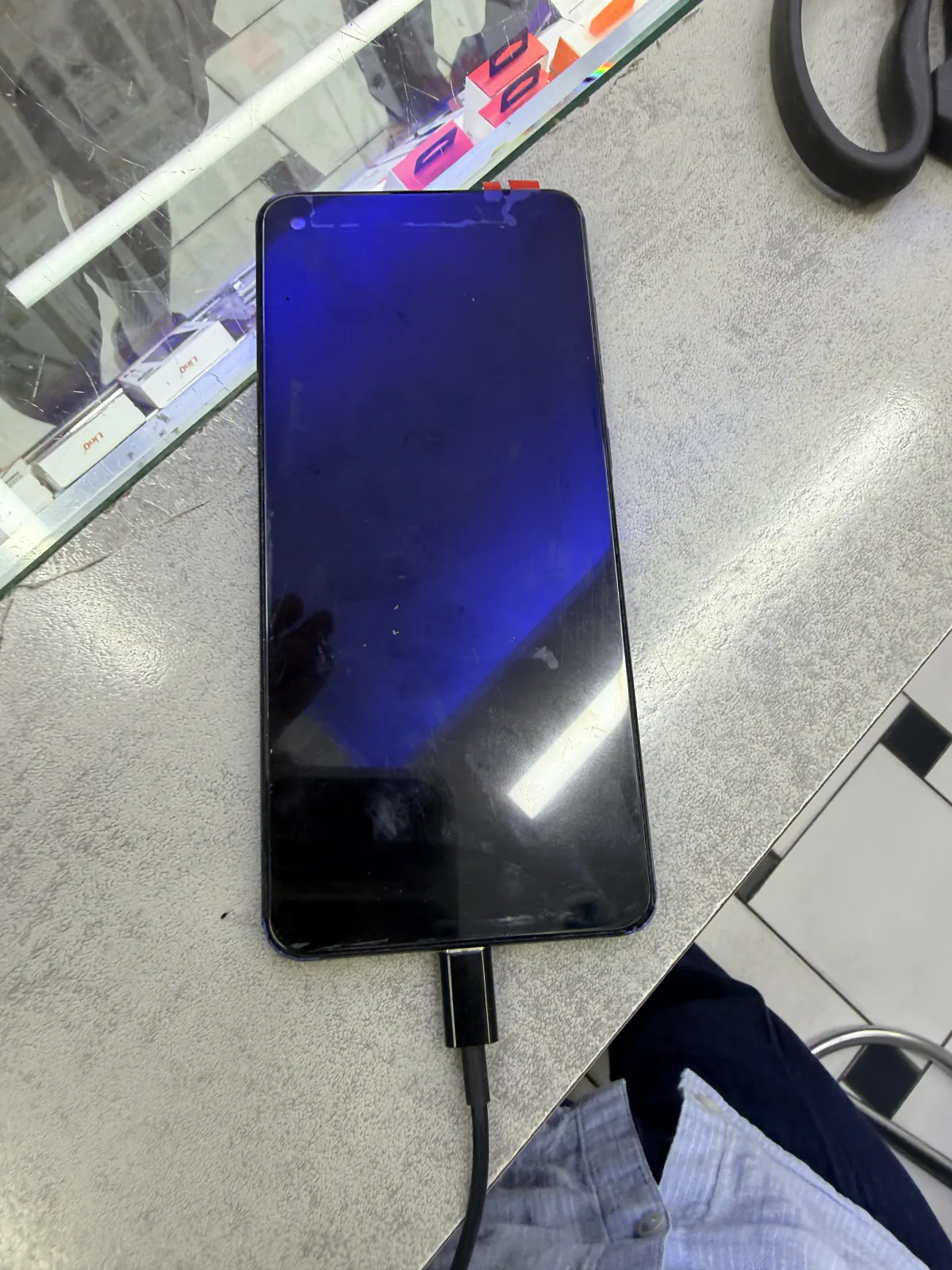 Smartphone display lit up blue, powered by a test cable before being fitted back into the phone
