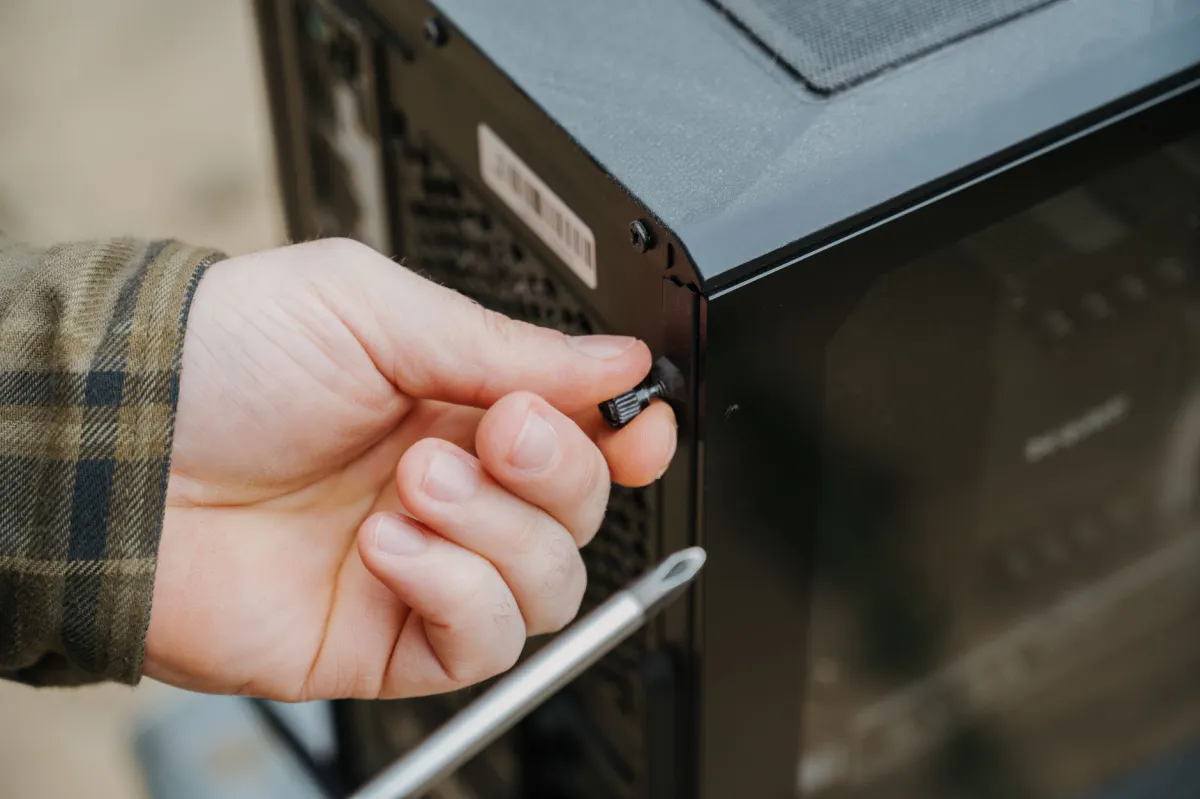 Hand holding a screwdriver, unscrewing a thumbscrew on the side panel of a black PC case