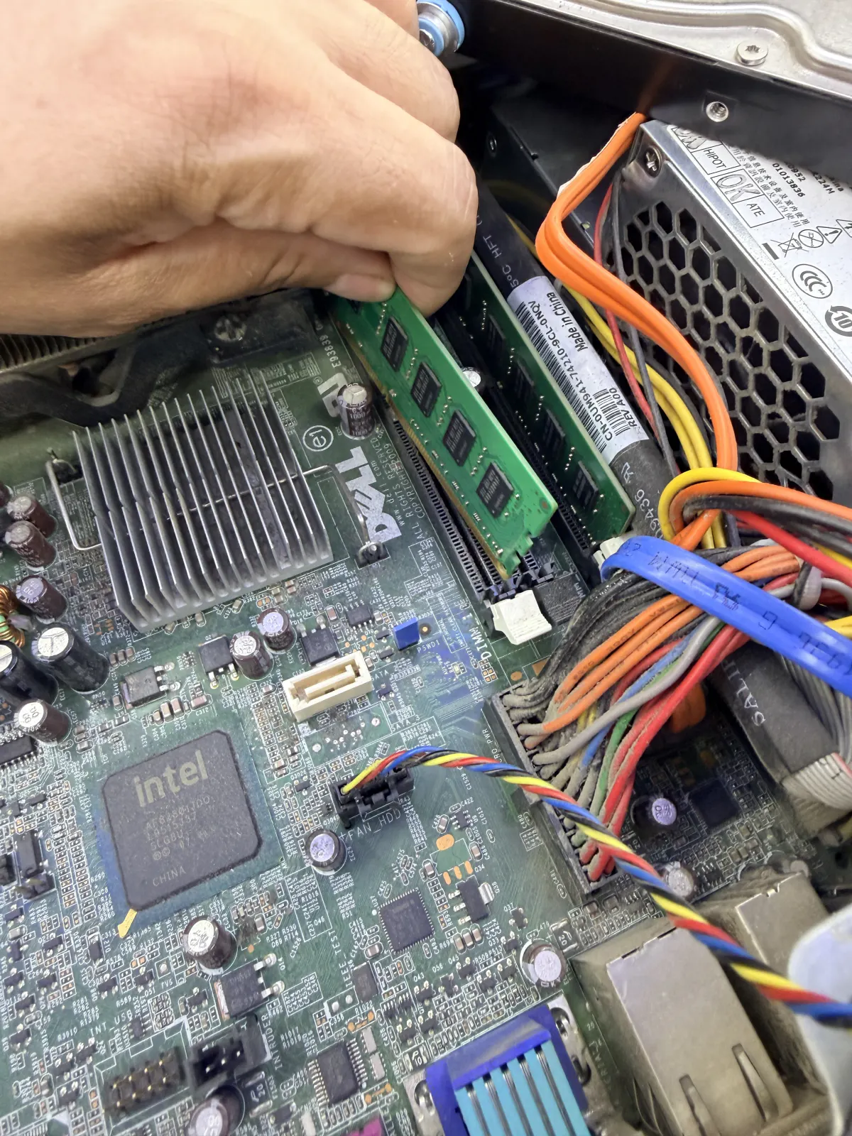 Installing a RAM stick into a Dell desktop, technician's hand pressing the module into the DIMM slot
