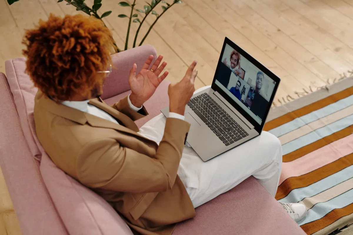 Personne assise sur un canapé, ordinateur portable sur les genoux, en visioconférence avec trois collègues visibles à l'écran